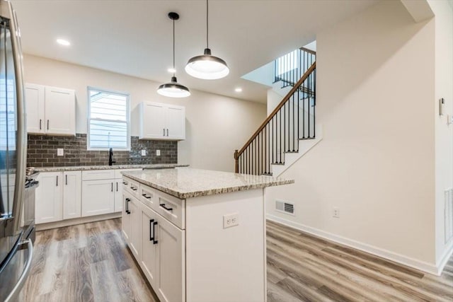 kitchen featuring a kitchen island, stainless steel refrigerator, decorative light fixtures, white cabinets, and light stone countertops