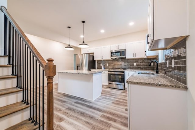 kitchen featuring appliances with stainless steel finishes, decorative light fixtures, sink, white cabinets, and a center island