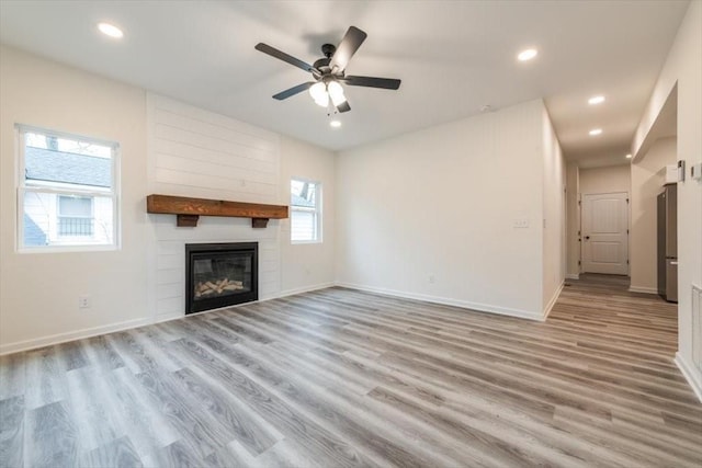 unfurnished living room with a large fireplace, ceiling fan, and light hardwood / wood-style flooring