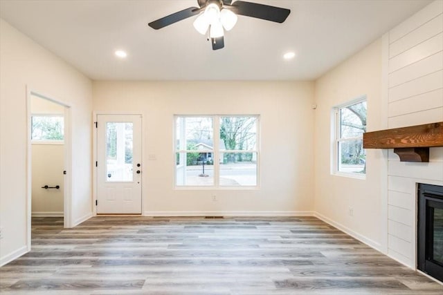 unfurnished living room with ceiling fan, a large fireplace, and light hardwood / wood-style floors