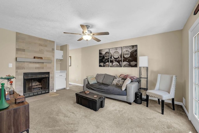 living room featuring baseboards, light colored carpet, a tile fireplace, a textured ceiling, and a ceiling fan