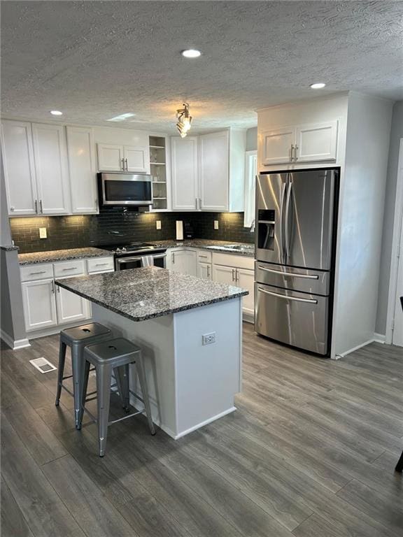 kitchen featuring tasteful backsplash, dark wood finished floors, a center island, white cabinetry, and stainless steel appliances