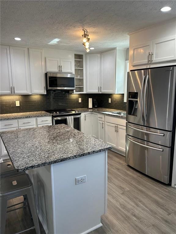 kitchen featuring tasteful backsplash, wood finished floors, a center island, white cabinetry, and stainless steel appliances