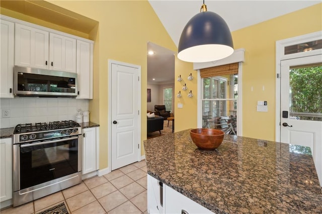 kitchen with decorative backsplash, appliances with stainless steel finishes, dark stone counters, white cabinetry, and hanging light fixtures