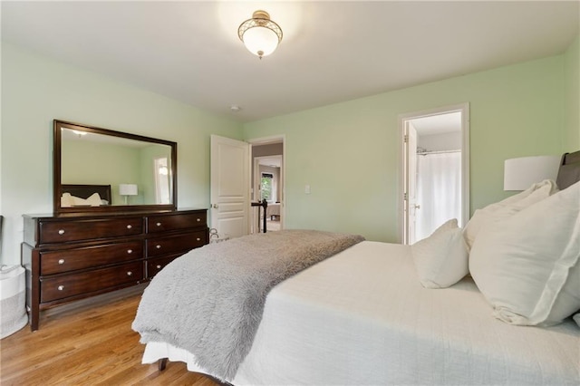 bedroom with light wood-type flooring, multiple windows, and connected bathroom