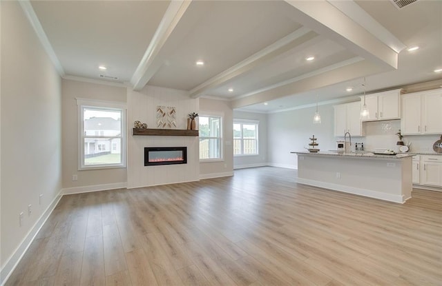 unfurnished living room with crown molding, baseboards, beam ceiling, light wood-style floors, and a glass covered fireplace