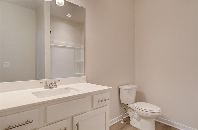 bathroom featuring baseboards, toilet, wood finished floors, and vanity