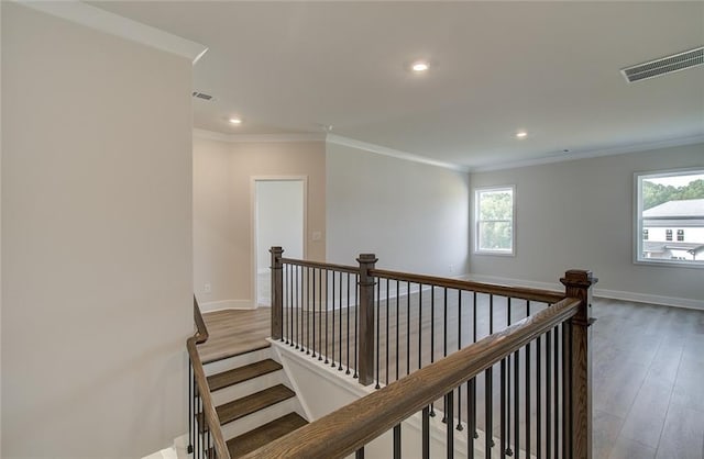 corridor featuring wood finished floors, visible vents, baseboards, crown molding, and an upstairs landing