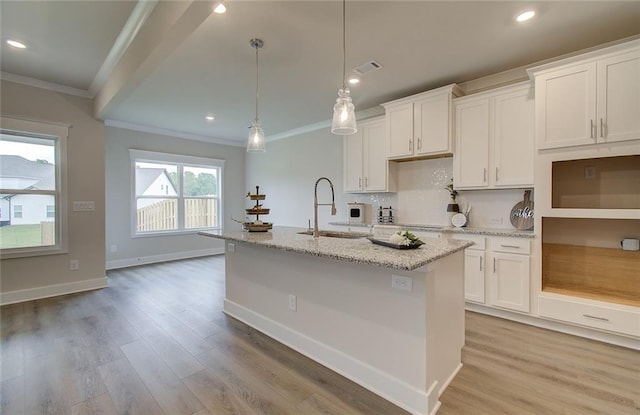 kitchen with a center island with sink, crown molding, light wood-style floors, and a sink