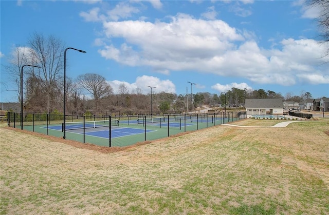 view of tennis court with a lawn and fence