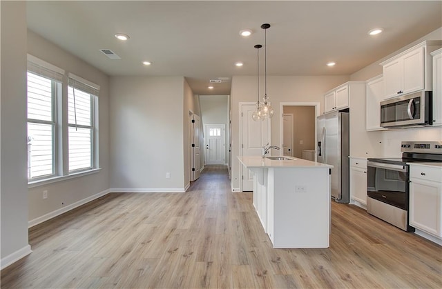 kitchen with appliances with stainless steel finishes, light hardwood / wood-style flooring, pendant lighting, white cabinets, and an island with sink