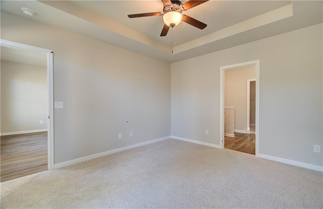 carpeted empty room featuring ceiling fan and a raised ceiling