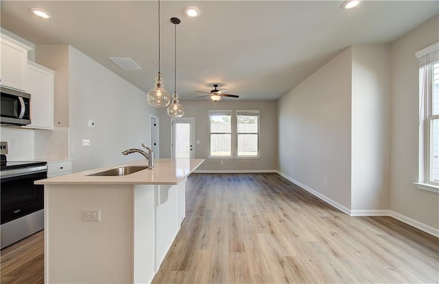 kitchen featuring sink, decorative light fixtures, stainless steel appliances, white cabinets, and an island with sink