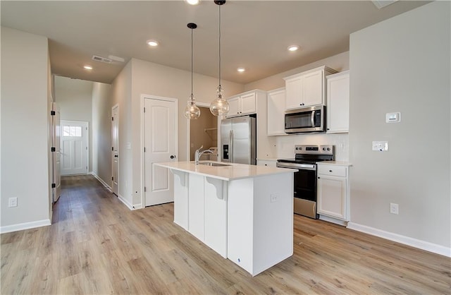 kitchen featuring appliances with stainless steel finishes, hanging light fixtures, an island with sink, white cabinets, and light wood-type flooring