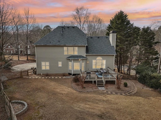 back house at dusk with a lawn and a deck