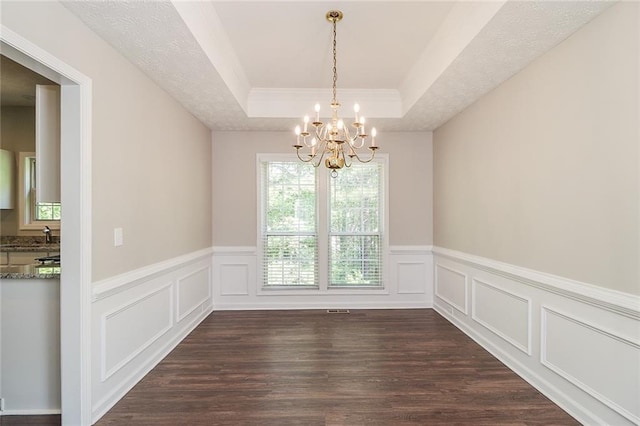 unfurnished dining area featuring dark wood finished floors, a wainscoted wall, a tray ceiling, ornamental molding, and a notable chandelier
