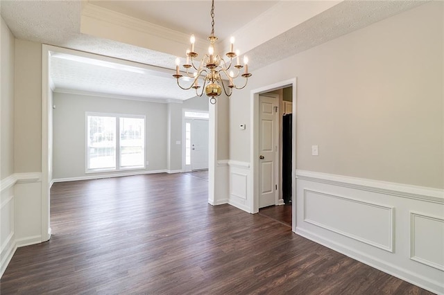 unfurnished dining area with a tray ceiling, wainscoting, a notable chandelier, dark wood-type flooring, and ornamental molding