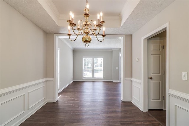 unfurnished dining area with a tray ceiling, dark wood-style flooring, crown molding, and a notable chandelier