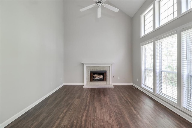 unfurnished living room with high vaulted ceiling, a ceiling fan, dark wood-style flooring, and a fireplace with raised hearth