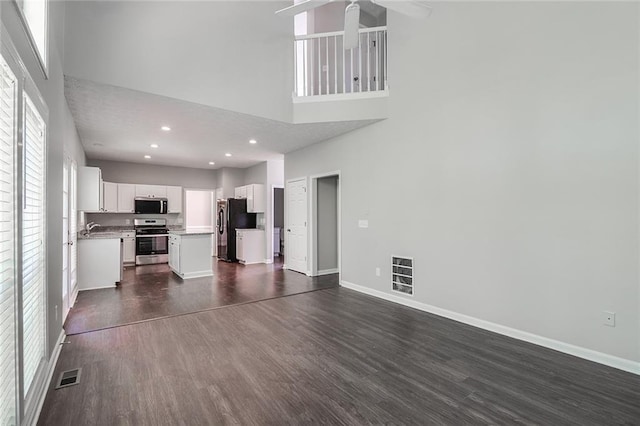 unfurnished living room featuring a towering ceiling, a ceiling fan, dark wood-type flooring, and visible vents