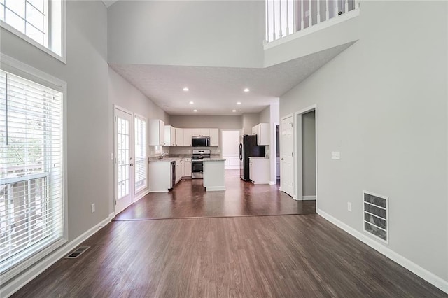unfurnished living room featuring dark wood finished floors, visible vents, a towering ceiling, and baseboards