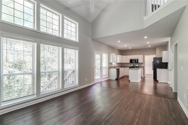 unfurnished living room with high vaulted ceiling, dark wood finished floors, and baseboards
