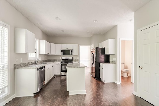 kitchen featuring white cabinets, stainless steel appliances, a sink, dark wood finished floors, and a kitchen island