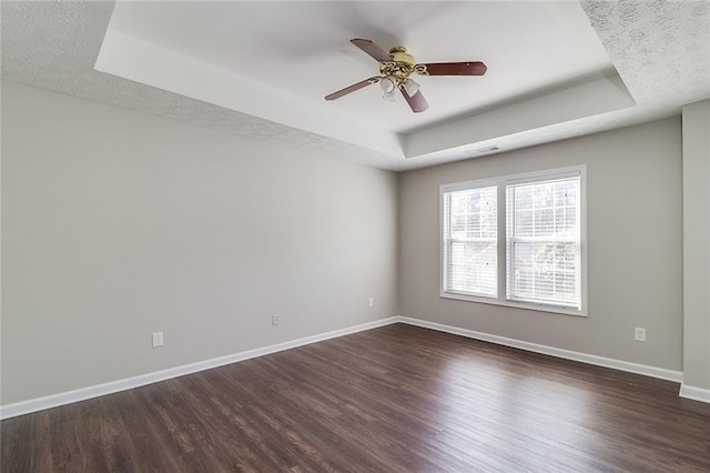 spare room with ceiling fan, a raised ceiling, baseboards, dark wood-type flooring, and visible vents