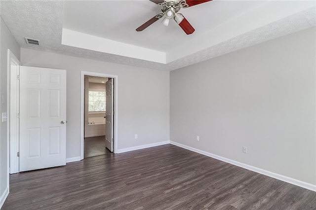 unfurnished bedroom featuring baseboards, visible vents, a raised ceiling, and dark wood-style flooring