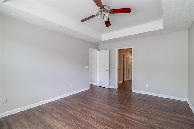 empty room with a ceiling fan, baseboards, a raised ceiling, and dark wood-style flooring