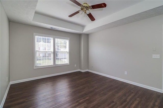 empty room with a tray ceiling, baseboards, and dark wood-type flooring