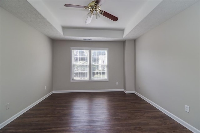 unfurnished room with ceiling fan, a tray ceiling, dark wood finished floors, baseboards, and visible vents