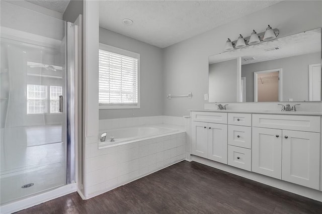 full bath featuring a textured ceiling, double vanity, wood finished floors, a shower stall, and a garden tub
