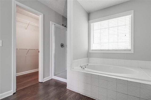 bathroom featuring a shower stall, a spacious closet, wood finished floors, a bath, and a textured ceiling