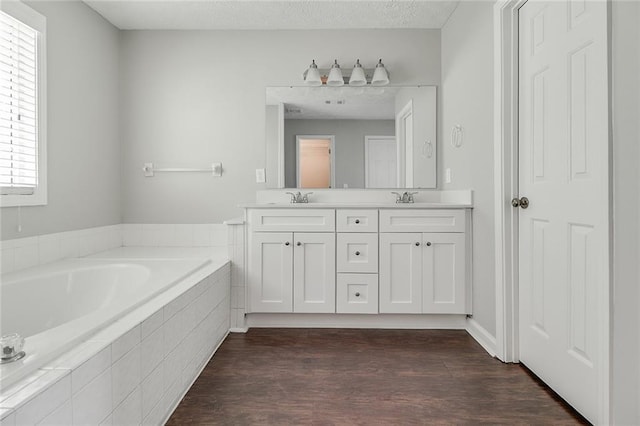 full bathroom featuring a garden tub, wood finished floors, a sink, and double vanity