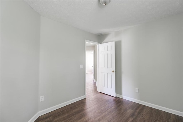 empty room featuring dark wood-type flooring, a textured ceiling, and baseboards