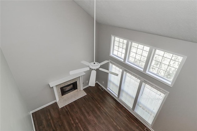 unfurnished living room with a high end fireplace, ceiling fan, a towering ceiling, dark wood-style flooring, and visible vents