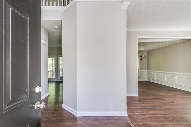 hallway with a wainscoted wall, a textured ceiling, a chandelier, wood finished floors, and ornamental molding