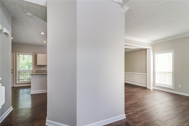 hallway featuring a textured ceiling, ornamental molding, baseboards, and dark wood-style flooring