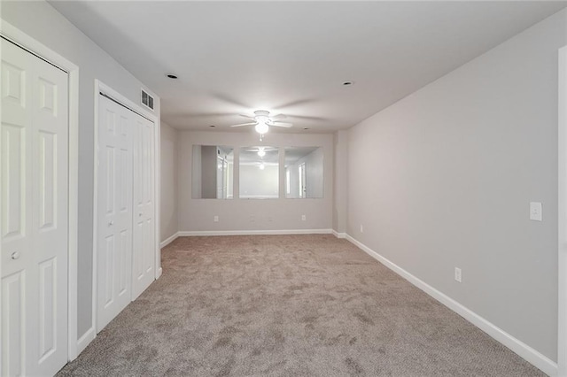 unfurnished bedroom with a ceiling fan, multiple closets, light colored carpet, baseboards, and visible vents
