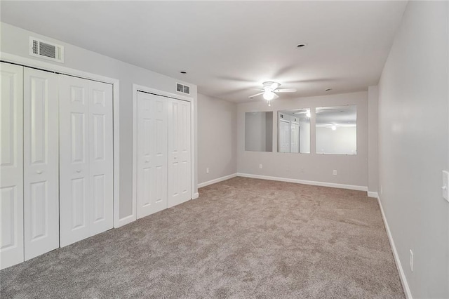 unfurnished bedroom with baseboards, multiple closets, visible vents, and carpet