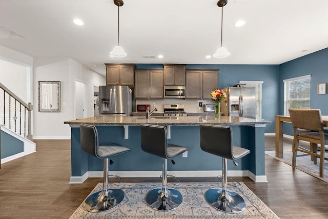 kitchen featuring appliances with stainless steel finishes, a breakfast bar, dark wood finished floors, and an island with sink