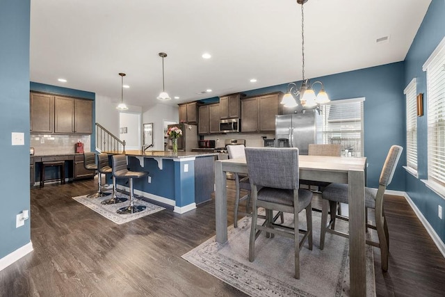 kitchen with dark wood-style floors, backsplash, an inviting chandelier, appliances with stainless steel finishes, and a kitchen breakfast bar