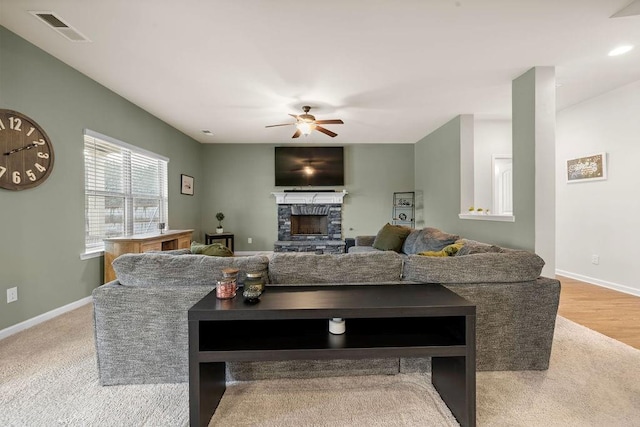 living room featuring baseboards, visible vents, a ceiling fan, and a stone fireplace