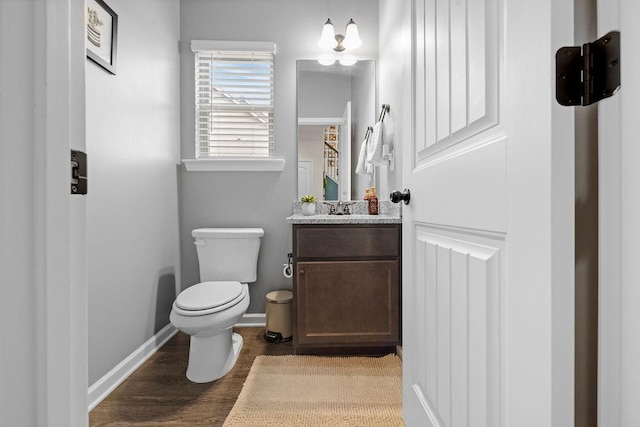 half bathroom with vanity, wood finished floors, toilet, and baseboards