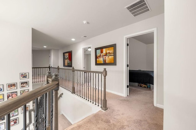 corridor with carpet, baseboards, visible vents, and an upstairs landing