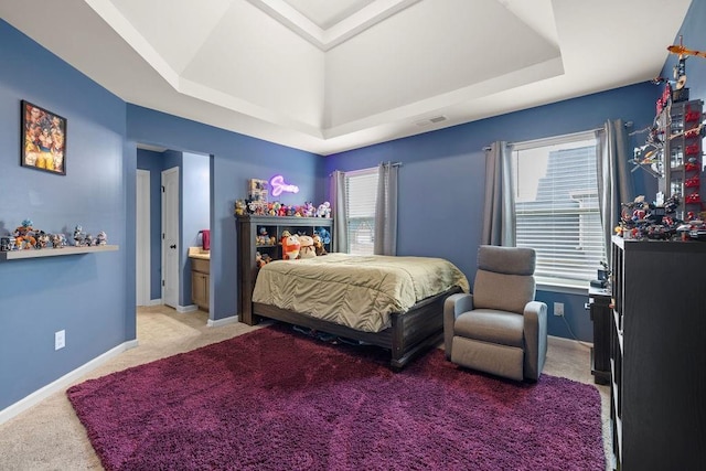 bedroom with a tray ceiling, light colored carpet, visible vents, ensuite bathroom, and baseboards