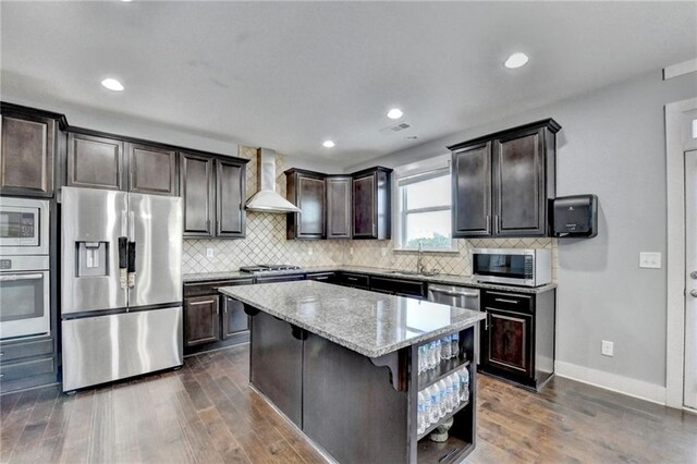 kitchen with a kitchen bar, wall chimney exhaust hood, stainless steel appliances, dark wood-type flooring, and a kitchen island