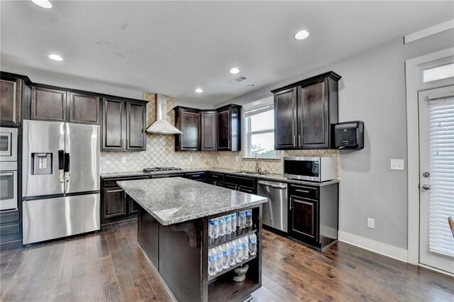 kitchen featuring dark wood-type flooring, a kitchen island, stainless steel appliances, and wall chimney range hood