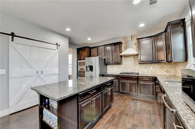 kitchen featuring dark hardwood / wood-style flooring, stainless steel appliances, wall chimney range hood, a barn door, and a center island